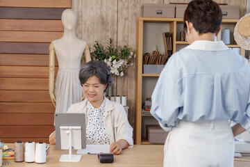 Senior asian tailor using tablet pos system while adult asian female client waiting after...