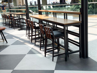 Tall wooden tables with high stools arranged by large windows in a public lounge. Representation of travel lifestyle, dining, and social atmosphere in modern hospitality spaces.