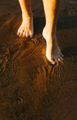 Barefoot woman walking through shallow sea water at sunset