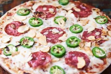 Pizza with salami, mozzarella cheese and jalapeno pepper. Wooden background. Soft focus.	