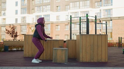 Strong willed trainee jumps onto wooden plyo box then jumps down during intense outdoor workout in urban park showcasing explosive power balance and fitness focus under clear sky city backdrop - Powered by Adobe