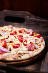Pizza with ham, salami, cherry tomatoes and mozzarella cheese. Rustic wooden background. Soft focus. Close up.	
