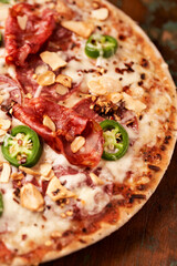 Pizza with salami, mozzarella cheese and jalapeno pepper. Wooden background. Soft focus.	