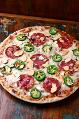 Pizza with salami, mozzarella cheese and jalapeno pepper. Wooden background. Soft focus.	