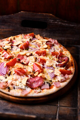 Pizza with ham, salami, cherry tomatoes and mozzarella cheese. Rustic wooden background. Soft focus. Close up.	