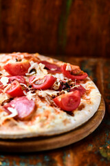 Pizza with ham, salami, tomatoes and mozzarella cheese. Rustic wooden background. Soft focus. Close up.	