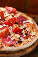 Pizza with ham, salami, cherry tomatoes and mozzarella cheese. Rustic wooden background. Soft focus. Close up.	