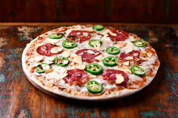 Pizza with salami, mozzarella cheese and jalapeno pepper. Wooden background. Soft focus.	