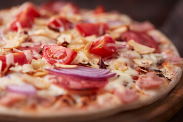 Pizza with ham, salami, cherry tomatoes and mozzarella cheese. Rustic wooden background. Soft focus. Close up.	