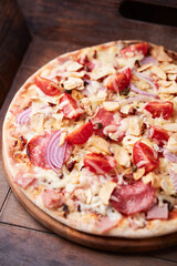 Pizza with ham, salami, cherry tomatoes and mozzarella cheese. Rustic wooden background. Soft focus. Close up.	