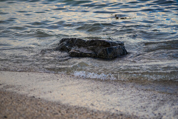 Single Black Rock in Ocean Waves on Sandy Beach Shoreline