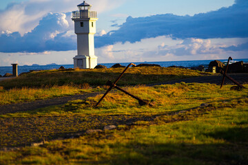 White Lighthouse with Old Anchors on Icelandic Coast at Sunset