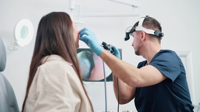 An otolaryngologist examines a patient. The doctor examines the nose of a young woman using a special camera. The therapist looks at the monitor screen.