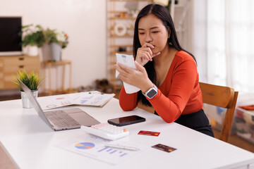 Sad Asian woman looking at many counts taxes on calculator credit cards in her hand and worried about loan debt pay late.
