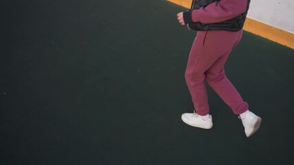 High angle view of legs of fitness enthusiast jogging around curved barbed wire sports court under pastel dusk sky, white sneakers stepping on asphalt adjacent to yellow edged barrier panels - Powered by Adobe