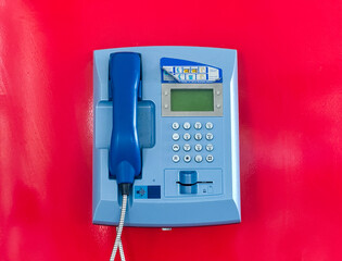 Blue public telephone on a red wall in a modern building. Communication, technology, and public service equipment for contact and emergency use in an airport interior.