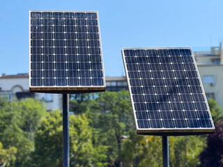 Two solar panels face the bright sky surrounded by green trees and buildings. Renewable energy, sustainability, and technology emphasize innovation, environment, and modern urban development.