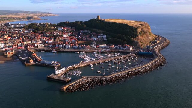 Aerial video of Scarborough Harbour in the morning light, with yachts docked in the marina and Scarborough Castle standing on the headland above the North Sea.