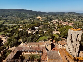 Panoramic view of rolling Tuscan hills with vineyards, olive groves, and medieval stone structures...