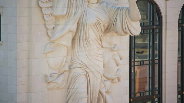 Pan Up on Angel Statue With Gold Horn on Side of Building in Urban City
