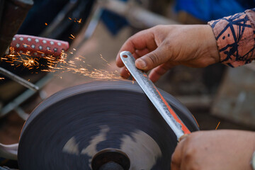Hands of craftsman shaping iron rod with sparks flying from rotary grinder