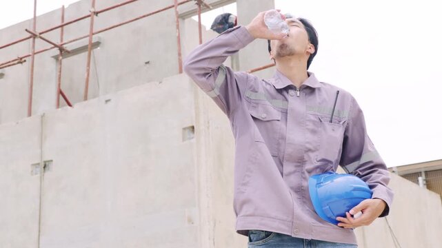 Asian male worker, plumber working outdoors construction site in a hot and humid residential building taking break to drink water to refresh himself.