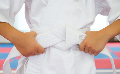 Close-up of a martial artist wearing a traditional white uniform (gi) and tying a white belt around the waist.