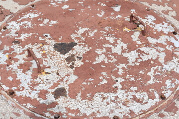 Septic tank lid closeup. Red and white paint chipped and worn from exposure to elements.