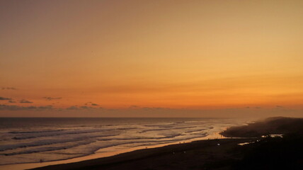 Obraz premium Scenic tropical beach sunset with golden sky, ocean waves and silhouettes of people along the coastline