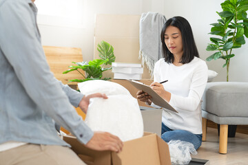Happy woman checking stuff in cardboard box before sent to transportation company and moving to new...