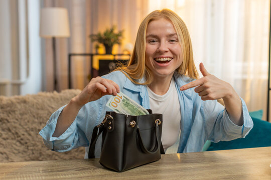 Young woman discovers finding hidden money dollar cash in small hand bag showing surprise amazement and joy. Caucasian girl on sofa marvels at new funds, reflecting delight over sudden financial boost