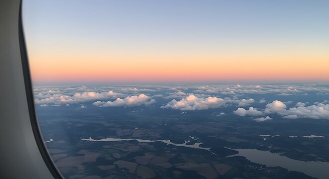 Aerial view of clouds and land at sunset from an airplane window creating beautiful scenic landscape