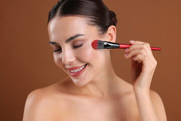 Fototapeta premium Beautiful woman applying makeup with brush on brown background