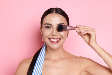 Beautiful woman with makeup brush on pink background
