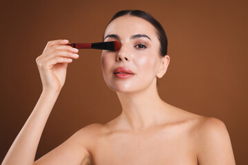 Obraz premium Beautiful woman with makeup brush on brown background