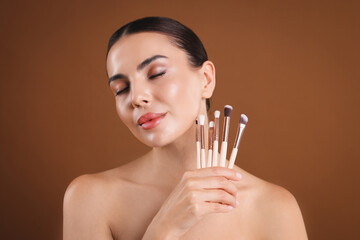 Beautiful woman with makeup brushes on brown background