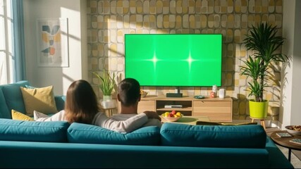 Couple watching a green screen tv in a cozy living room, bathed in warm sunlight from the window - Powered by Adobe