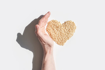 Caucasian male hand protecting heart shaped oats against light background showing health and...