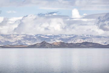 Panorama landscape of Lake Karakul in the Pamir mountains in the Tien Shan against the background of high snowy rocky peaks with clouds, morning panorama of the lake for the background