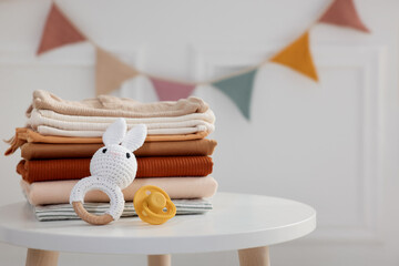 Stack of clean baby clothes and accessories on white table indoors, closeup. Space for text