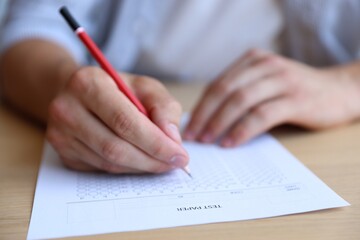 Student filling out multiple choice test at wooden table, closeup. Passing exam