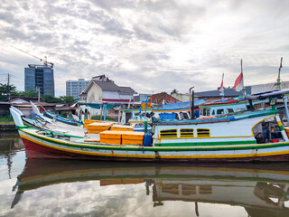 Traditional fishing boat docked at a riverside pier with bright colors reflecting on calm water,...