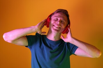 Smiling man wearing headphones listening to music in neon lights against orange background