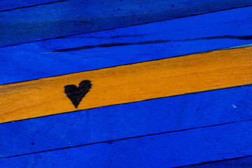 Horizontal pattern of blue and orange painted wooden planks with a black heart symbol drawn on the orange plank, creating a vibrant abstract background.