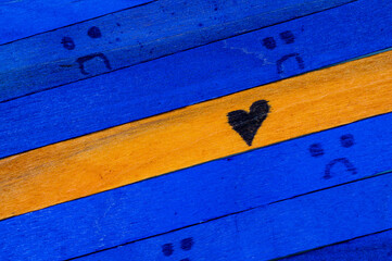 Orange wooden stick with a black heart symbol among blue sticks with sad faces, emotional contrast...
