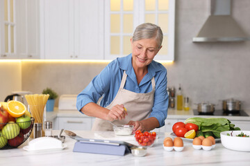 Senior woman cooking at white marble table in kitchen