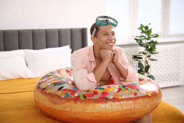 Happy man with diving mask and inflatable ring on bed at home. Dreaming about vacation at sea