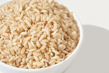 Bowl of raw whole grain brown rice on white background with natural light.
