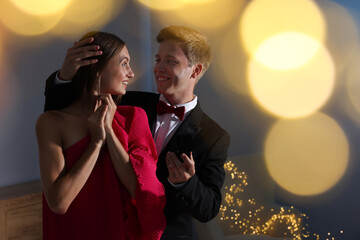 Making marriage proposal. Smiling man with engagement ring surprising his girlfriend in dark room, space for text. Bokeh effect