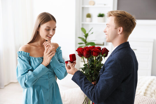 Man with engagement ring and bouquet of roses making marriage proposal to his happy girlfriend at home
